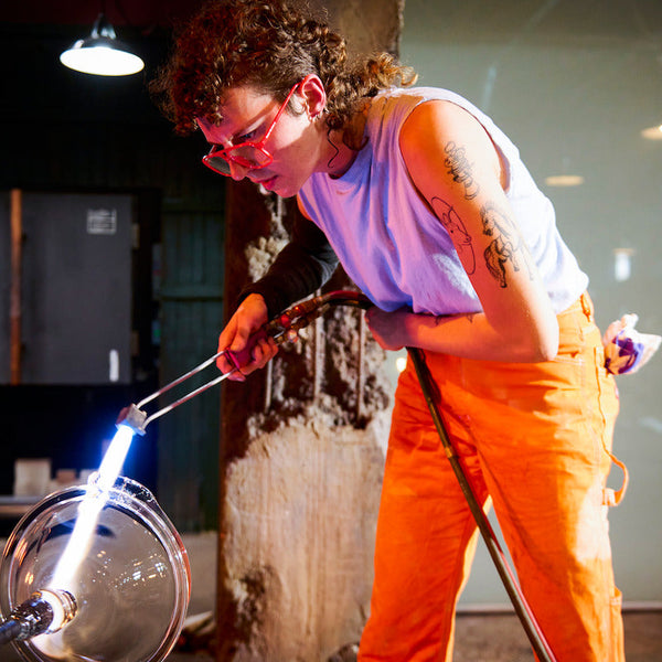 Person working with glassblowing tools in a workshop setting